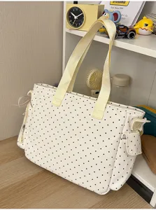 Sac crème à pois noirs et anses jaune pâle, posé sur une table en bois près d'une étagère.