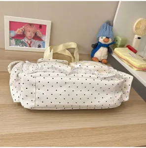Sac blanc à pois noirs, bordure en dentelle et anses beige posé sur une table en bois