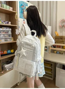 Vue de dos d’une élève avec un sac blanc à étoiles, rayures et pendentif étoilé en chambre
