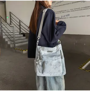 Sac bandoulière bleu clair à étoiles, porté de côté, avec breloque argentée et poches zippées