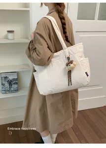 Une personne porte un grand sac écru avec breloque ourson, devant une étagère et une porte blanches