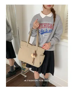 Modèle avec cabas beige à longues anses, poche latérale et breloque ourson, en intérieur