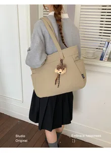 Vue de dos d’un modèle portant un cabas beige avec un porte-clés ourson et un ruban à carreaux