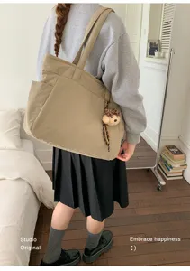 Une personne porte un cabas beige à poche latérale et pendentif ours en peluche dans un intérieur