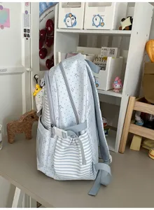 Vue latérale d’un sac à dos bleu clair à étoiles et points, poche rayée et bretelles