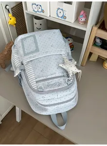 Vue en biais d’un sac bleu clair à petits motifs étoilés, côtés rayés et poche zippée à l’avant