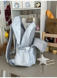 Gros plan d’un sac à dos ouvert bleu clair à étoiles, avec poche rayée et pendentif étoile suspendu