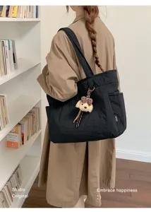 Vue de dos avec un grand sac noir porté à l’épaule et un pendentif ours en peluche beige