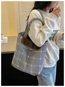 Eine Frau trägt eine blau-grau karierte Tasche mit braunen Details über der Schulter am Fenster