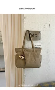 Sac kaki à poches multiples avec pendentif ours, devant un rideau clair et un mur texturé