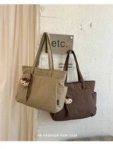 Sacs kaki et brun foncé suspendus au mur, avec poche extérieure et petit ours en peluche accroché.