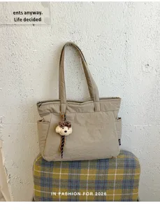 Sac beige devant un mur texturé, avec deux anses, des poches latérales et un petit ourson en peluche