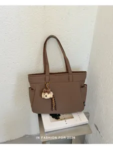 Sac cabas marron avec poches latérales et breloque en peluche, présenté sur une étagère métallique
