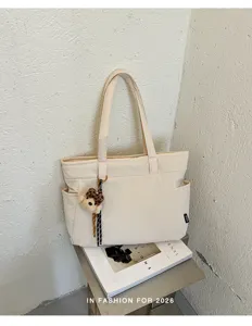 Sac en tissu ivoire à deux anses, orné d’un pendentif ourson et posé sur un magazine ouvert