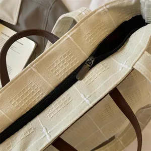 Cremefarbener Canvas-Shopper mit Karoprägung, dunkelbraunen Griffen und schwarzem Reißverschluss