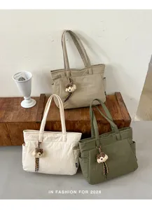 Trois sacs kaki, crème et vert olive avec des breloques ourson en peluche, sur une table en bois
