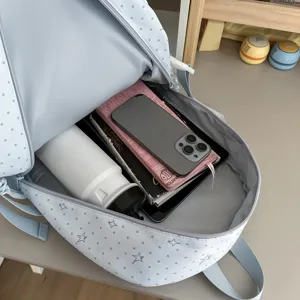 Sac à dos bleu clair à pois gris et étoiles, ouvert avec des objets du quotidien à l’intérieur