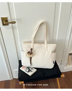 Sac crème texturé avec deux anses, poche latérale et breloque ours, posé sur une chaise noire
