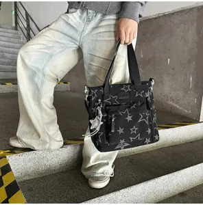 Une personne tient un sac noir à étoiles, avec poche zippée et breloque étoile argentée.