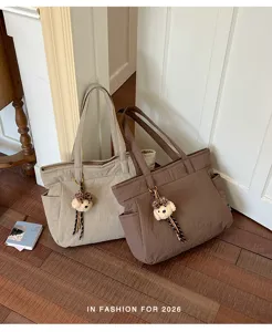 Deux cabas beige et marron, à longues anses et breloques ourson, posés sur un parquet en bois