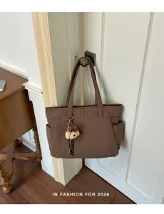 Sac brun suspendu par ses anses, avec un pendentif ourson en peluche et une poche latérale visible