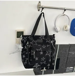 Sac cabas noir à étoiles grises, poche zippée, deux anses et breloque étoile argentée.