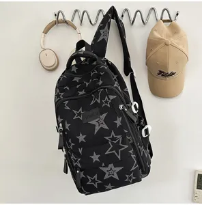 Sac noir à étoiles grises suspendu à un crochet mural, avec zip avant et bretelles visibles.