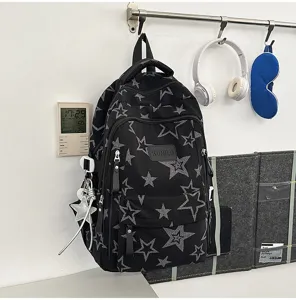 Sac à dos noir à étoiles, zips frontaux et breloque étoile, présenté devant un mur blanc.