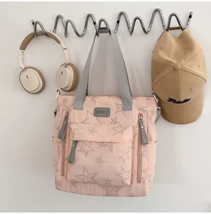Tissu rose à étoiles, anses grises, poches zippées devant et petite étiquette visible.