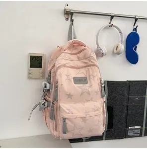 Sac à dos rose à étoiles grises, poches zippées devant, suspendu au mur près d’un casque audio.