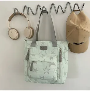 Sac vert clair à étoiles, poignées grises et plusieurs poches zippées à l’avant, suspendu au mur