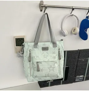 Sac vert clair suspendu au mur, avec imprimé d’étoiles grises, poches avant zippées et anses.