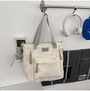 Sac en toile ivoire suspendu, avec étoiles grises, poches avant zippées et anses grises tissées.