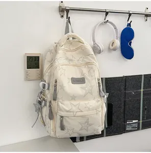 Détail des étoiles grises, du pendentif argenté et de l’étiquette avant sur le sac à dos crème