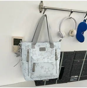 Sac bleu clair à étoiles suspendu au mur, avec anses grises, poches avant et étiquette KOMILO