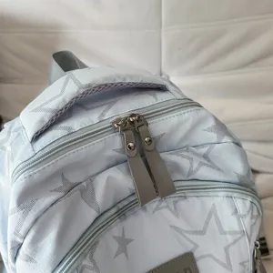 Sac à dos bleu clair à étoiles grises, double zip et poignée en maille, vu de près
