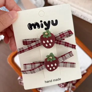 Close-up of two burgundy fabric strawberry clips with white dots, green leaves and plaid bows