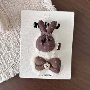 Detalle de pinzas de tela marrón con forma de conejo y lazo, ribete de encaje blanco y flor