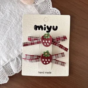 Two strawberry clips with white dots and green leaves, paired with red plaid bows on a display card