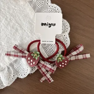 Flat lay of red elastic hair ties with strawberry appliqués, gold bead accents and plaid ribbon bows
