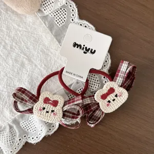 Close-up of red plaid bow hair ties with cream knitted bear faces, bows and rosy cheeks