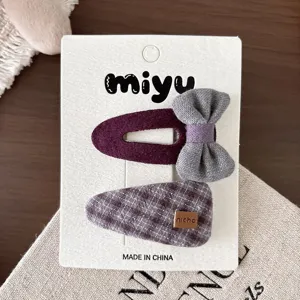 Dos pinzas de tela en una tarjeta: una ciruela con lazo gris y otra morada de cuadros