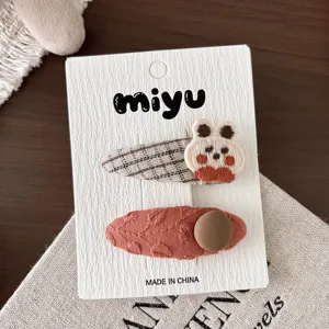 Pinzas de tela sobre una tarjeta: bordado de cuadros y pinza color óxido con detalle redondo beige