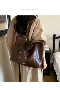 Rear view of a model carrying a brown tote with studded trim and a green fluffy charm indoors