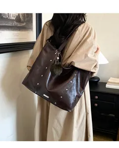Back view of a model carrying a dark brown faux leather tote with silver studs and a fluffy charm