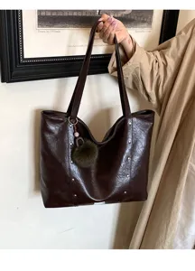 Hand-held close view of a glossy dark brown bag with stud accents, long straps, and a furry charm