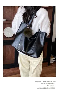 Back view of a black studded tote worn over a white sweater, with a fluffy pom-pom charm
