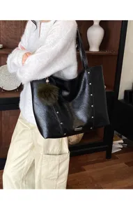 Lifestyle view of a model holding a black tote with metal studs and a dark green fur charm