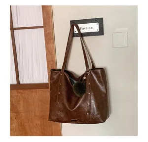 Brown faux-leather tote with long shoulder straps, stud details and a fluffy pom-pom charm