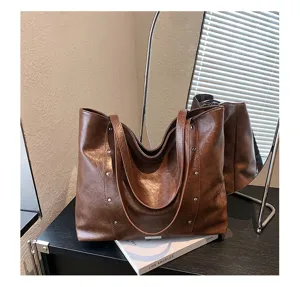 Brown faux-leather tote displayed on a table, showing rivet accents and its dual carry straps